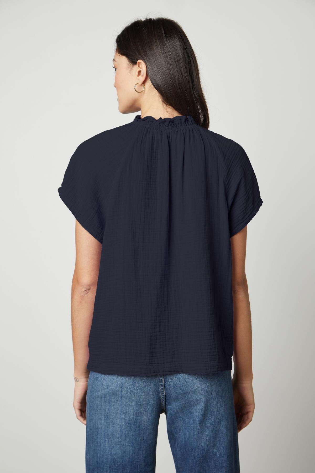 The back view of a woman wearing a Velvet by Graham & Spencer JADEN COTTON GAUZE V-NECK TOP and jeans.-35678664622273