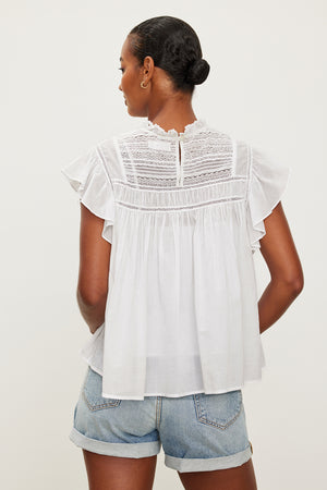 The back view of a woman wearing INESSA COTTON LACE TOP by Velvet by Graham & Spencer shorts and a white blouse.