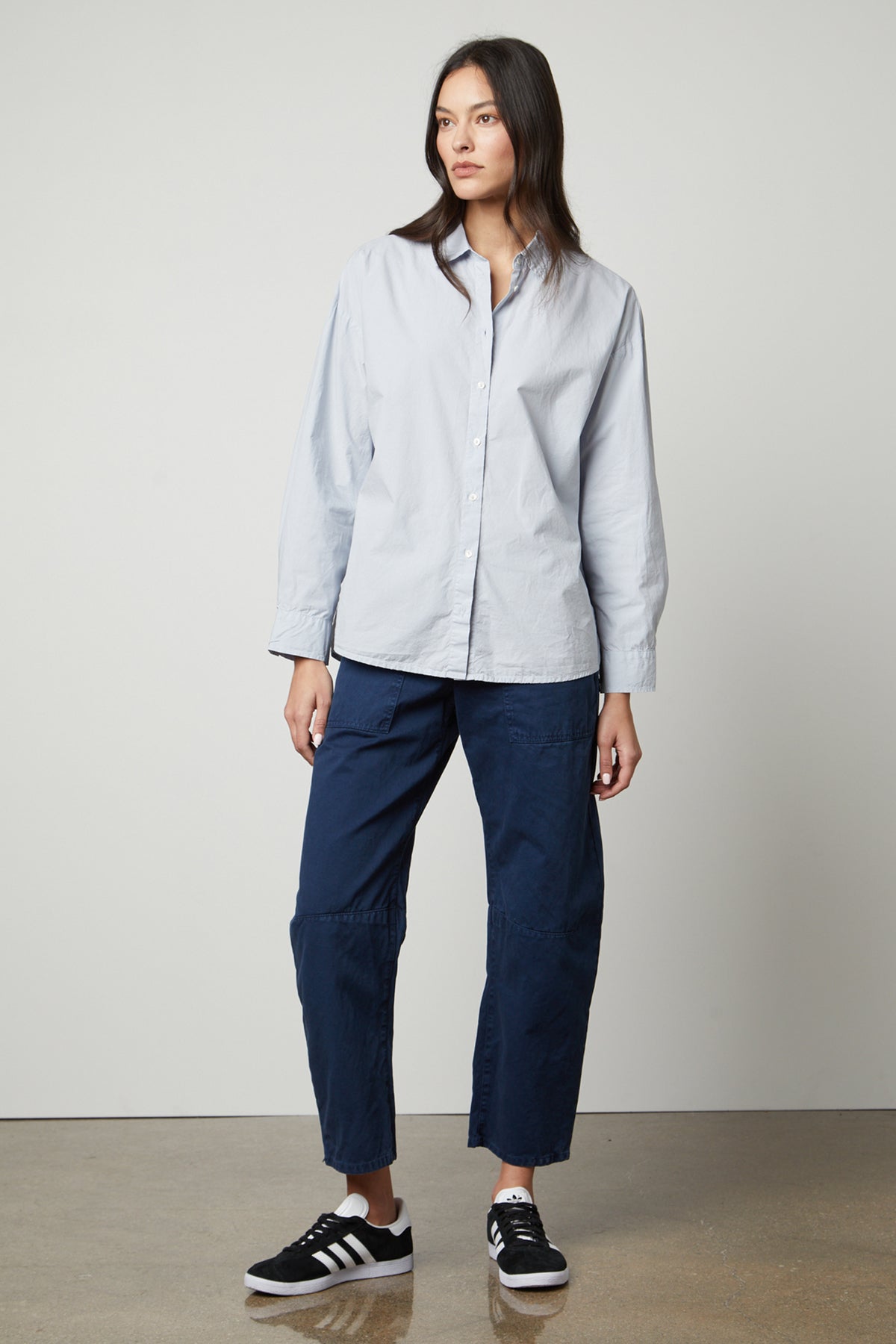 A woman wearing a Velvet by Graham & Spencer Dakota Button-Up Shirt and blue pants in a modern design.-26914845688001