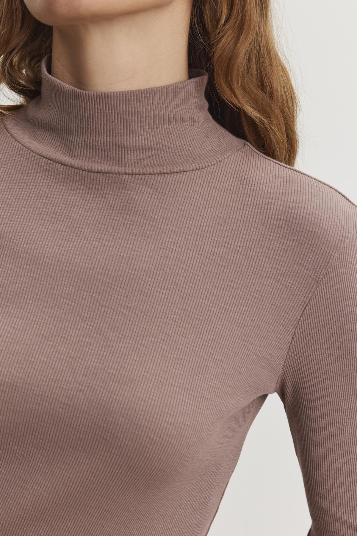 A person is wearing an ADRIAN TEE from Velvet by Graham & Spencer, which is a brown ribbed cotton slub turtleneck; their shoulder-length brown hair contrasts against a plain background.-38483543851201