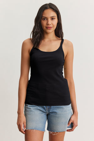Someone with long hair wearing the ALIZA Ribbed Cotton Layering Tank by Velvet by Graham & Spencer and denim shorts stands against a plain background.