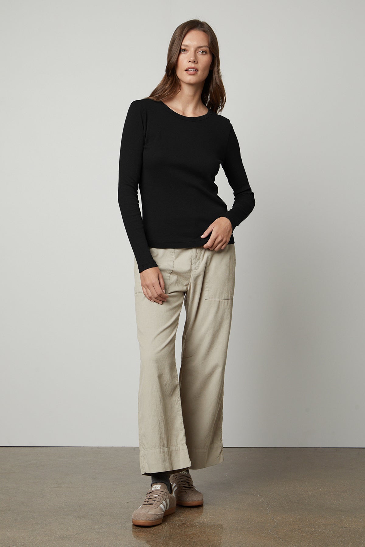 The model is wearing a black long-sleeved Velvet by Graham & Spencer BAYLER RIBBED SCOOP NECK TEE and beige wide leg pants.-35782696796353