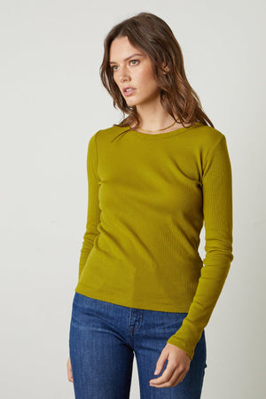A woman wearing a green Velvet by Graham & Spencer BAYLER RIBBED SCOOP NECK TEE sweater and jeans.