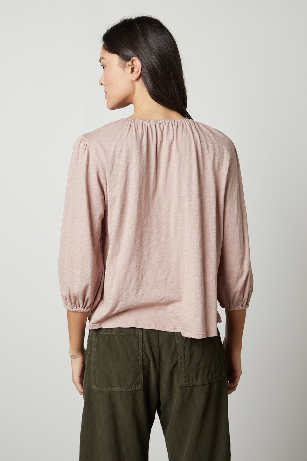 The back view of a woman wearing a Velvet by Graham & Spencer JULIE 3/4 SLEEVE TEE and green pants.