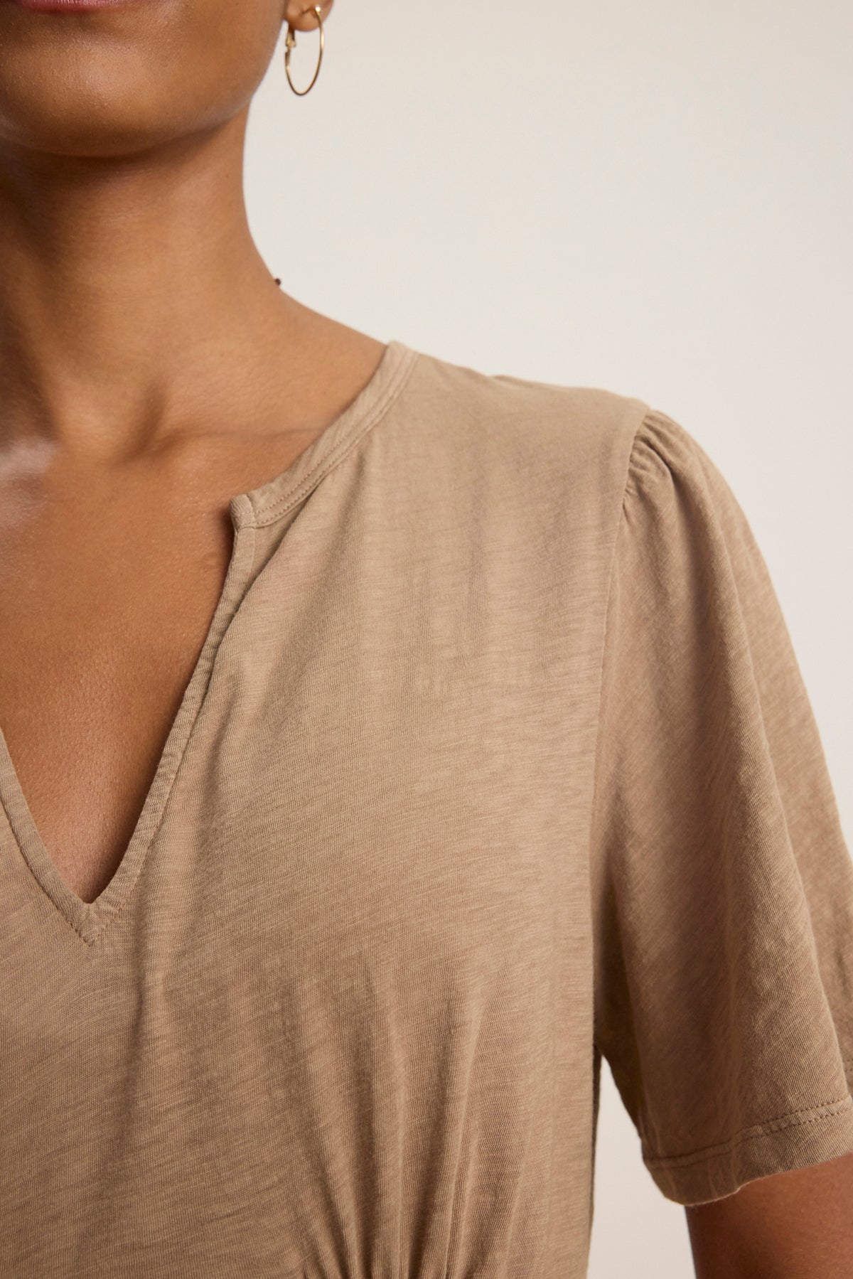 Close-up of a person wearing the MADELINE DRESS by Velvet by Graham & Spencer, featuring a light brown split neckline and short sleeves in soft cotton slub, with a single hoop earring visible.-39120014049473
