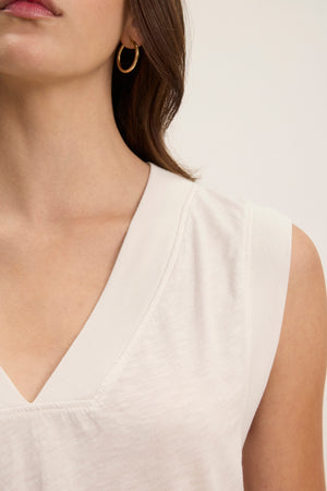 A woman wears the MARIA TEE by Velvet by Graham & Spencer—a white, textured cotton slub V-neck sleeveless top—with gold hoop earrings, shown from the shoulders up against a plain background.