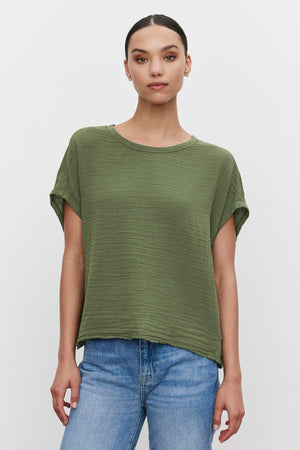 Young woman in a green CAROLINE COCOON TOP and blue jeans standing against a white background. Brand: Velvet by Graham & Spencer