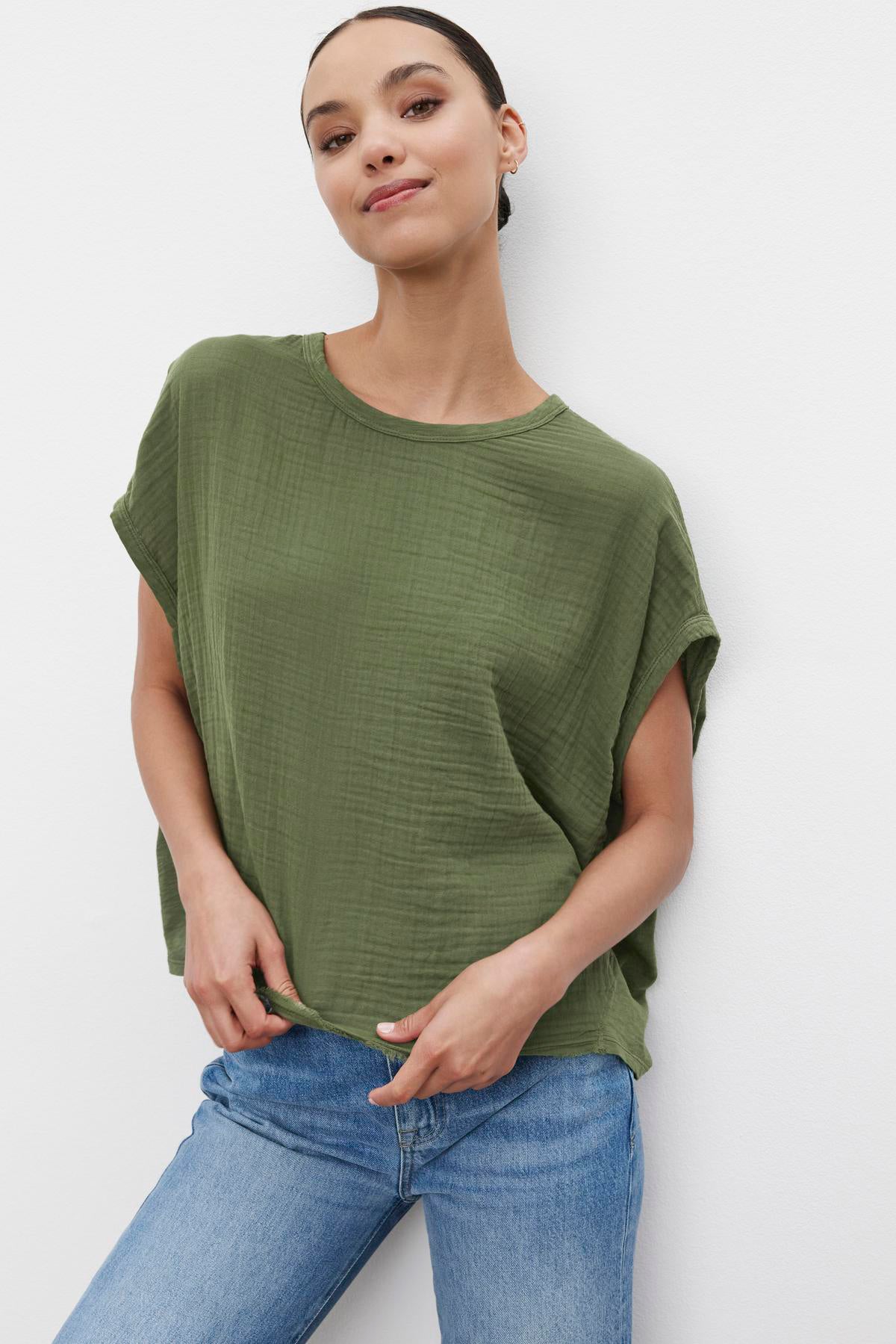 Woman in a Velvet by Graham & Spencer CAROLINE COCOON TOP and blue jeans standing against a white backdrop, with a confident posture and slight smile.