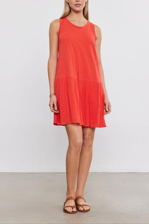 A woman wearing a Velvet by Graham & Spencer MINA DRESS with a tiered skirt and brown sandals stands against a plain white background.