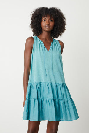 A woman wearing a Velvet by Graham & Spencer teal PAIGE TIERED DRESS with ruffles.