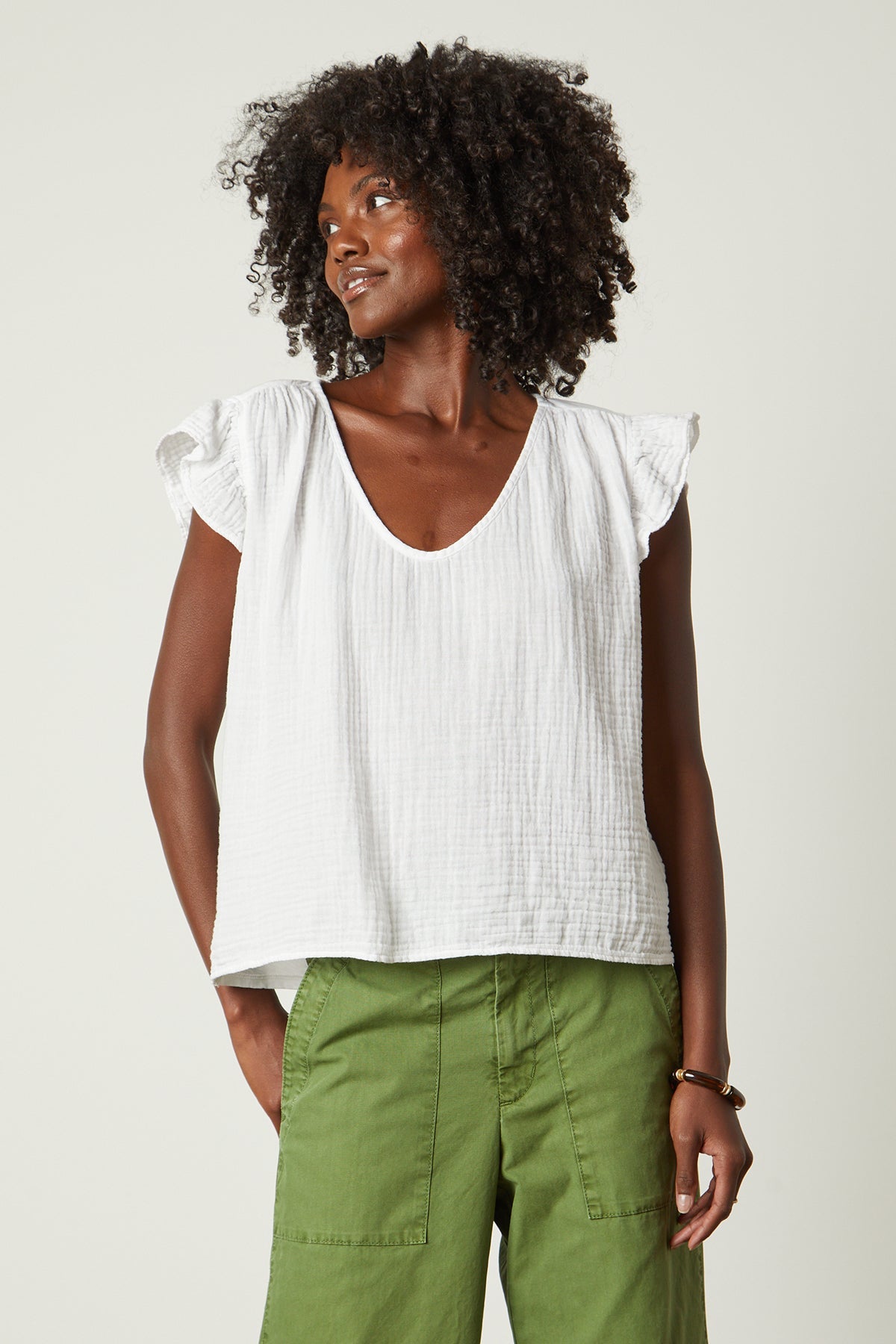 a woman wearing a Velvet by Graham & Spencer REMI RUFFLE SLEEVE TOP and green pants.