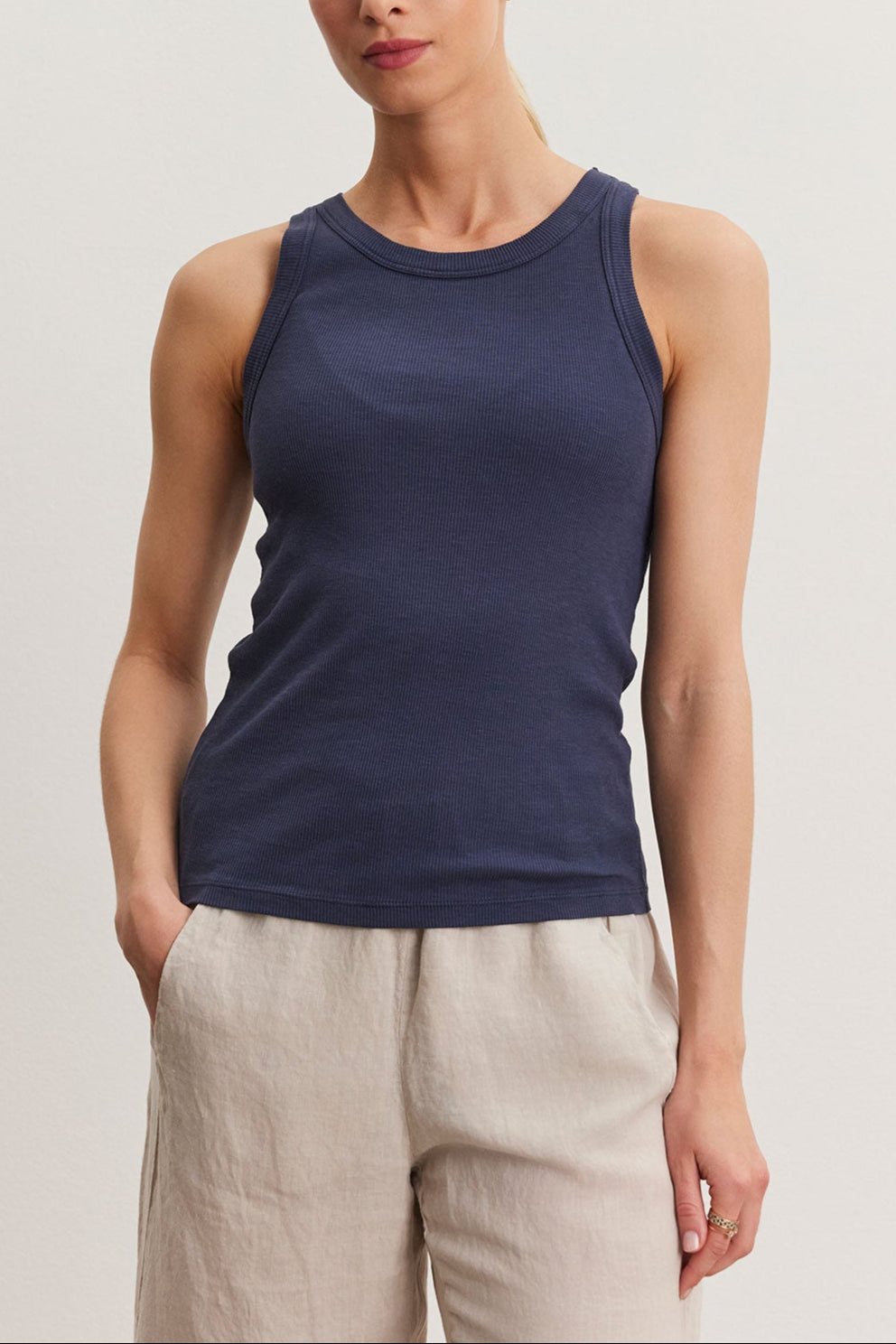 A woman in a navy blue Velvet by Graham & Spencer NOLA tank top and beige pants standing against a plain background.
