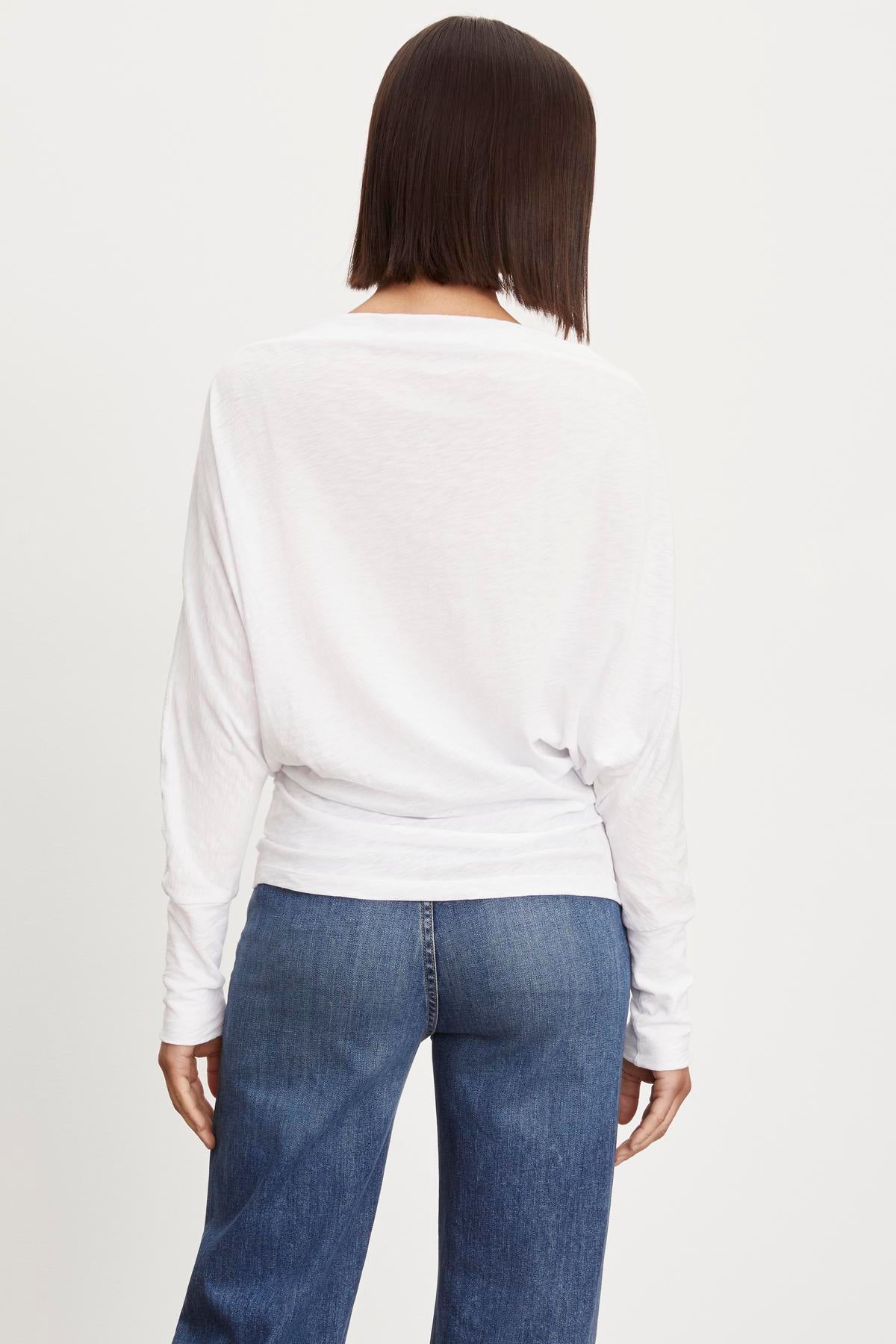 The view of a woman wearing Velvet by Graham & Spencer's NOVALEE DOLMAN TEE jeans and a white long sleeve top.