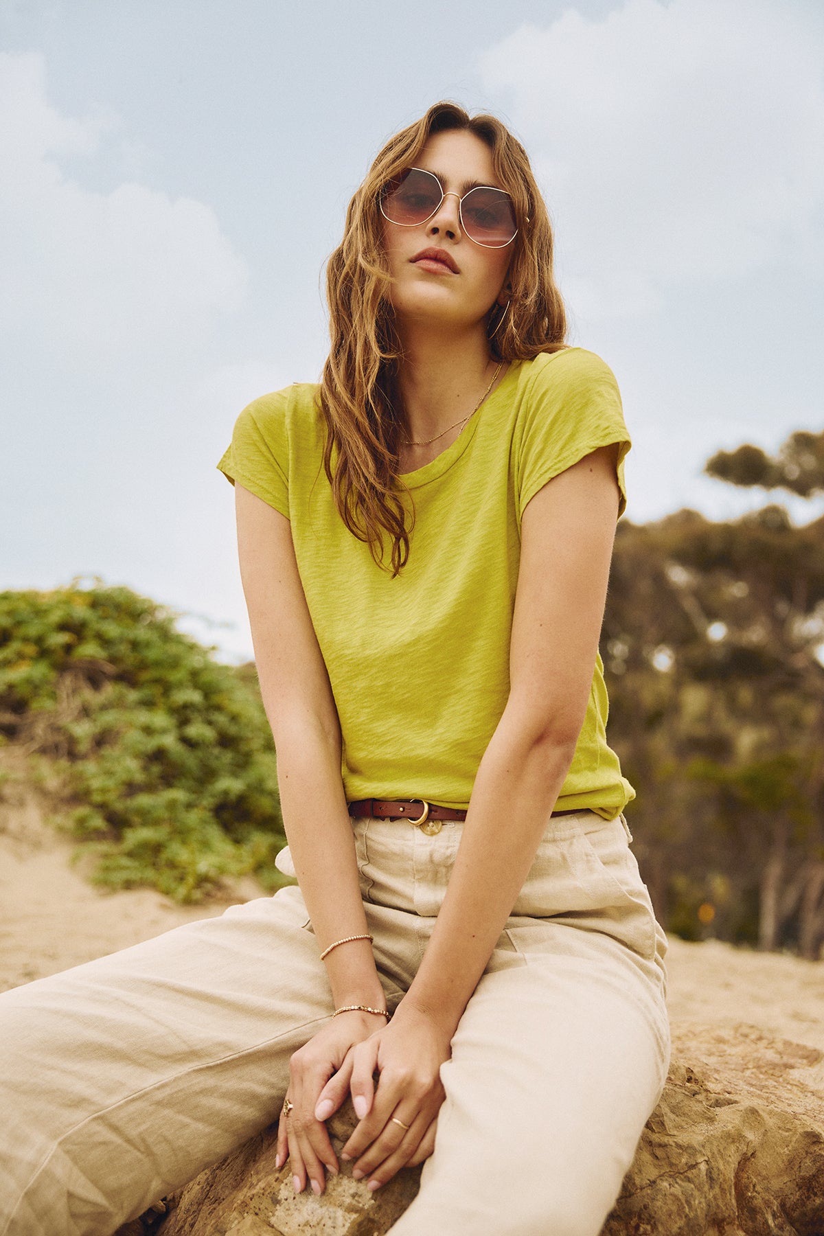 A woman in a yellow t-shirt sitting on a rock, wearing the DRU HEAVY LINEN PANT by Velvet by Graham & Spencer.