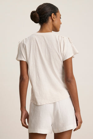 A woman faces away, hair in a bun, wearing the PAULA TEE by Velvet by Graham & Spencer— a light cotton slub crew-neck tee—paired with matching shorts against a neutral background.