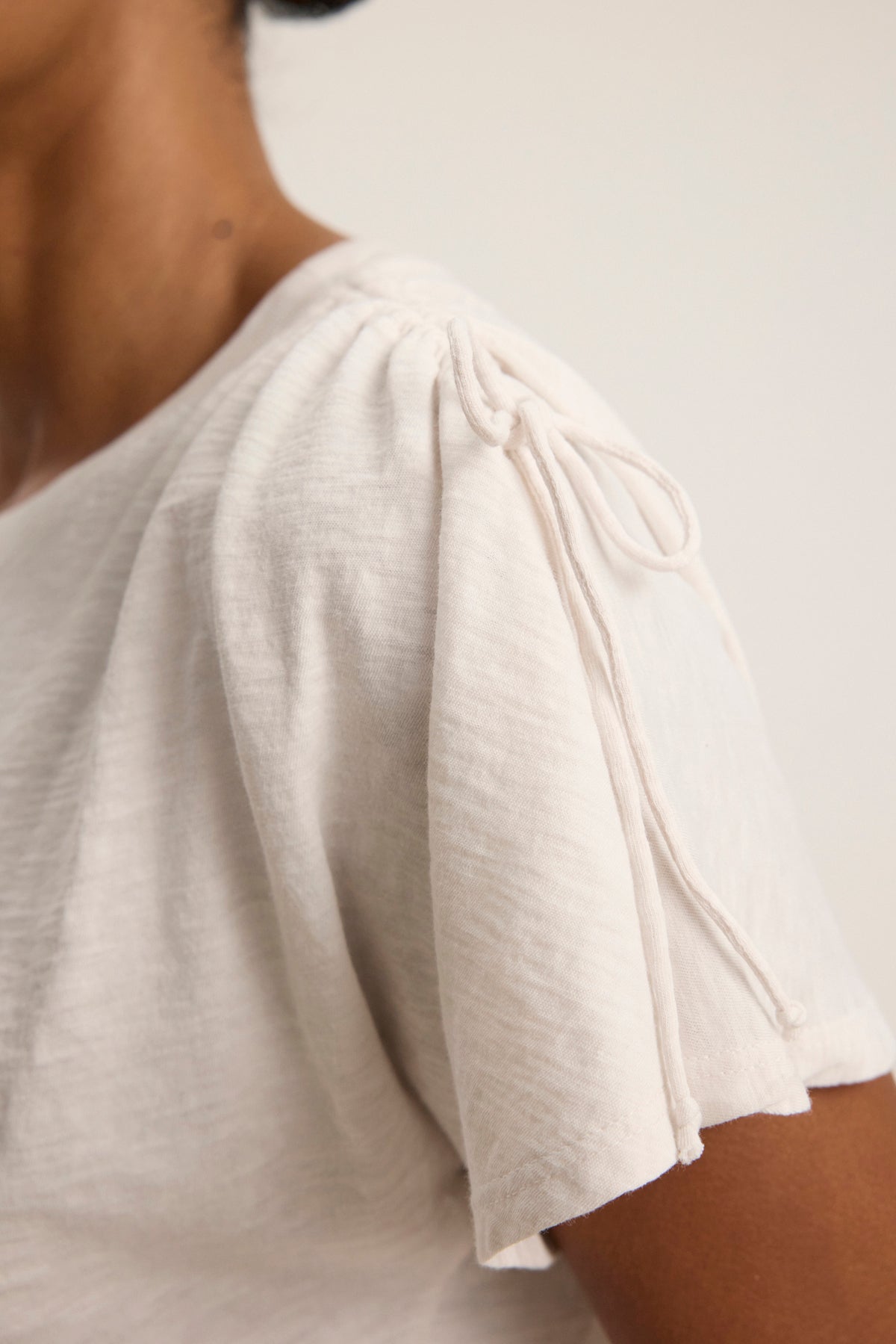 Close-up of a person wearing the PAULA TEE by Velvet by Graham & Spencer—a light cotton slub crewneck with gathered shoulders and a delicate bow accent at the seam.