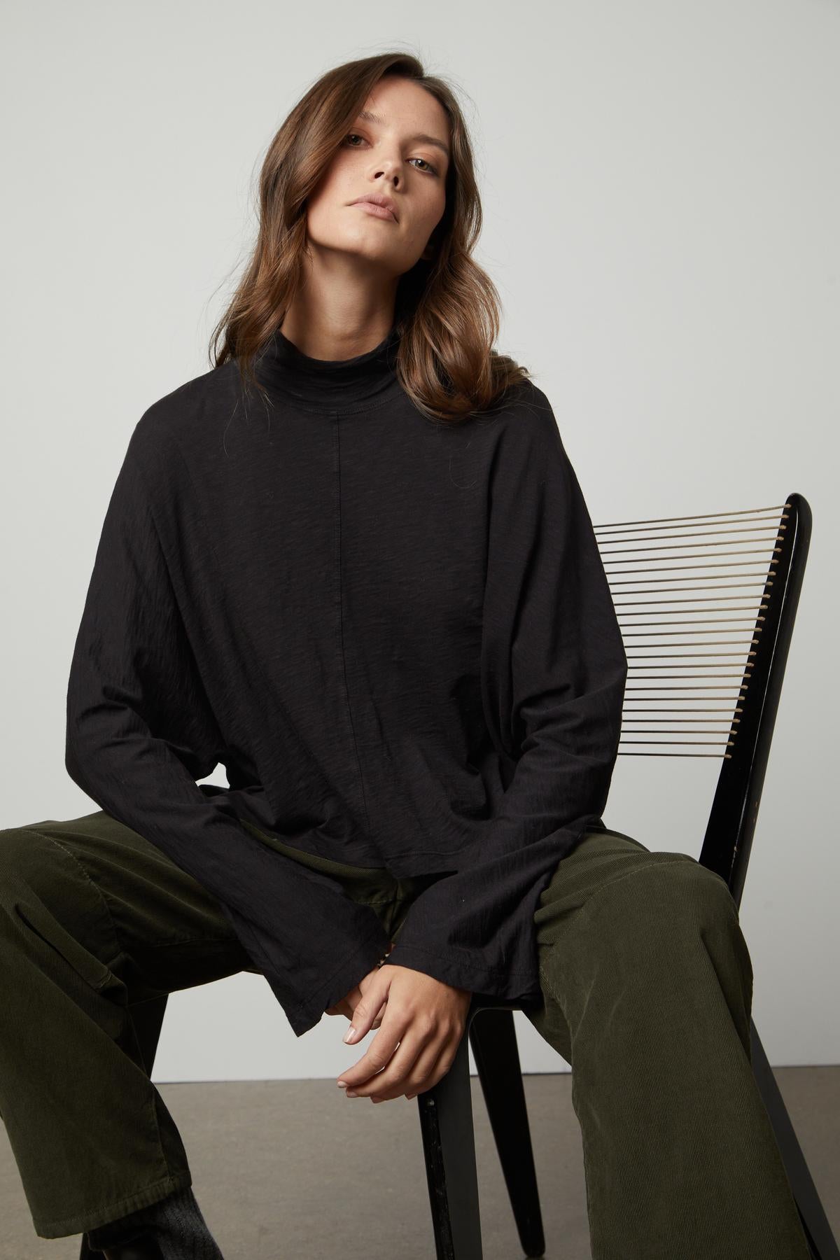 A person is sitting on a chair wearing a Velvet by Graham & Spencer STACEY MOCK NECK TEE.-26895469445313