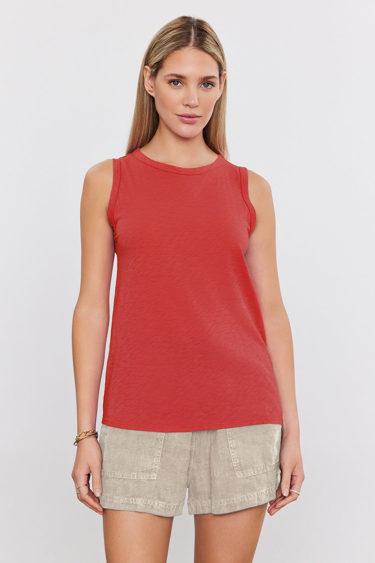 A person with long hair stands against a plain background wearing a timeless Velvet by Graham & Spencer TAURUS TANK TOP and beige shorts.-36909438599361