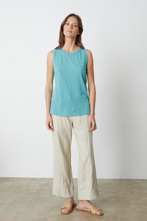 A woman standing in front of a white wall wearing a Velvet by Graham & Spencer TAURUS COTTON SLUB TANK with Dru Pant in sand full length front with sandals.