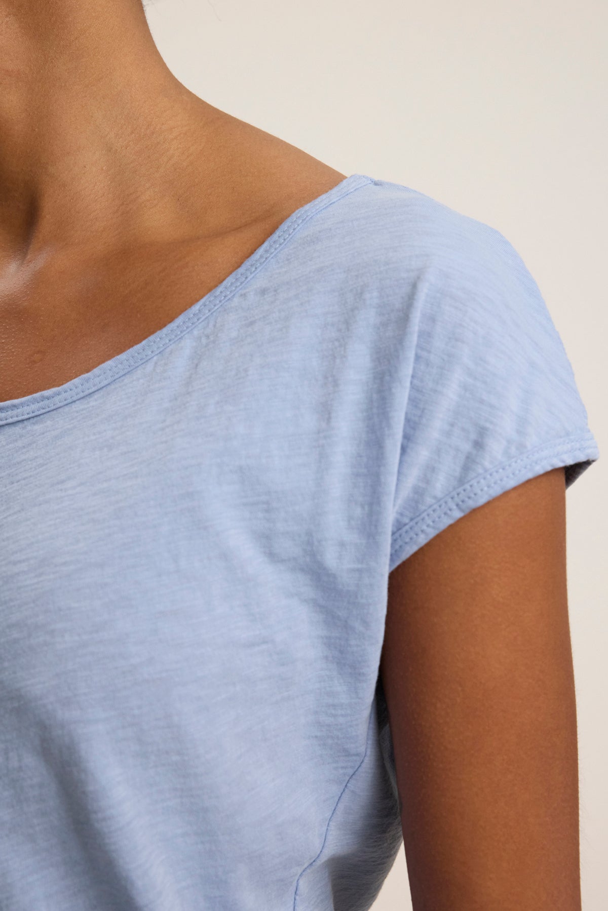 A close-up of a person wearing the VIVIENNE TEE by Velvet by Graham & Spencer in light blue, featuring a scoop neckline and short sleeves, made from soft cotton slub, against a plain background.