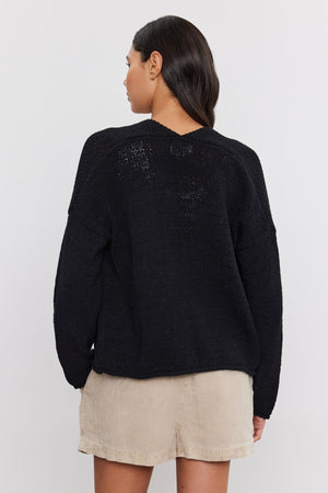 A woman seen from behind wearing a black textured knit HOLLIE CARDIGAN by Velvet by Graham & Spencer paired with beige shorts.