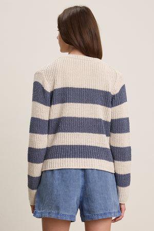 A person with straight brown hair is shown from the back wearing Velvet by Graham & Spencer’s MAXINE SWEATER—a cream and navy striped cotton blend crewneck—with blue denim shorts, against a neutral background.