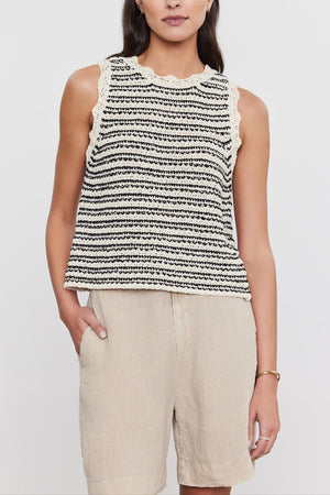 A woman wearing a Velvet by Graham & Spencer SOPHIE SWEATER VEST with scallop details and beige trousers, standing against a white background.