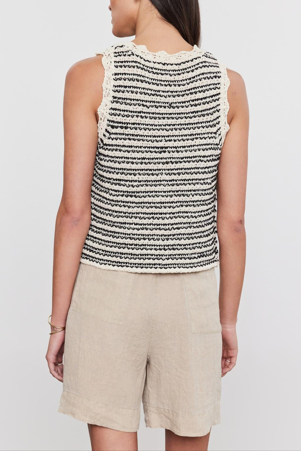 Woman standing with her back to the camera, wearing a black and white striped SOPHIE SWEATER VEST sleeveless top with a crew neckline and beige shorts by Velvet by Graham & Spencer.