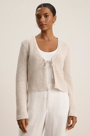 A woman wears the THALIA CARDIGAN by Velvet by Graham & Spencer, a cream-colored soft cotton cropped cardigan, over a white top and white pants against a plain light background.