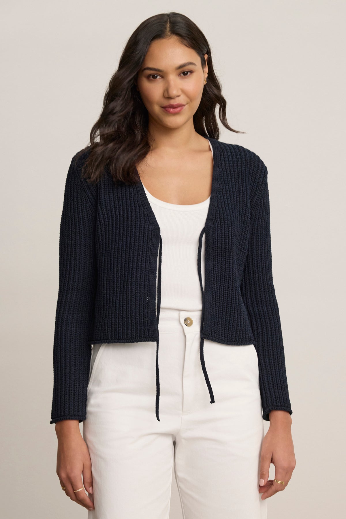 A woman faces forward, wearing the THALIA CARDIGAN by Velvet by Graham & Spencer in navy blue over a white top and white pants against a plain background.-39120167436481