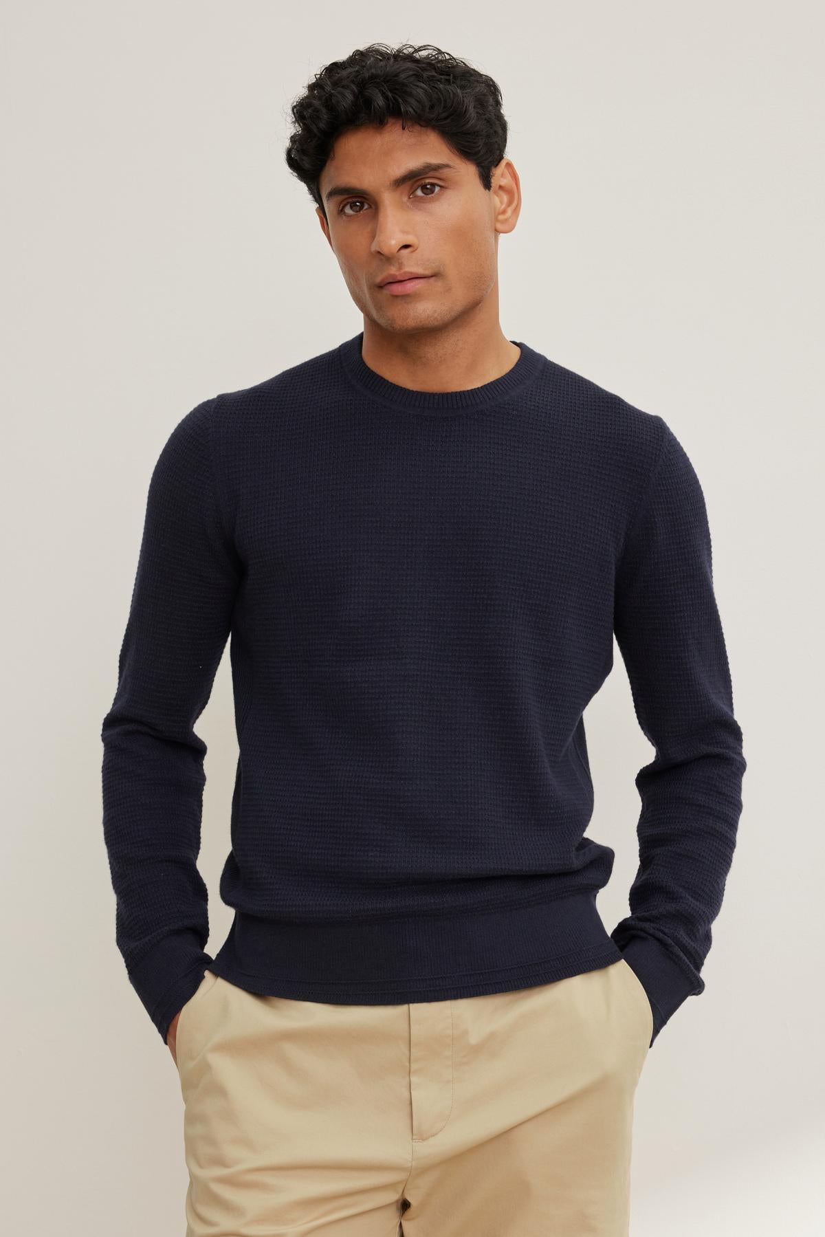 A person wearing the ACE COTTON CASHMERE THERMAL CREW by Velvet by Graham & Spencer and beige pants stands against a plain background, hands in pockets.-38643202326721