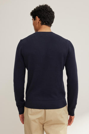 Someone with short curly hair is wearing a dark blue ACE COTTON CASHMERE THERMAL CREW by Velvet by Graham & Spencer and beige pants, standing with their back to the camera against a plain background.