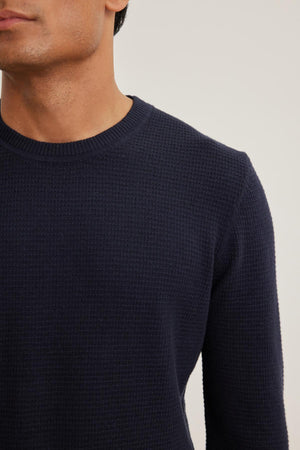 Close-up of an individual in a dark blue ACE COTTON CASHMERE THERMAL CREW by Velvet by Graham & Spencer, highlighting the upper body against a neutral background.