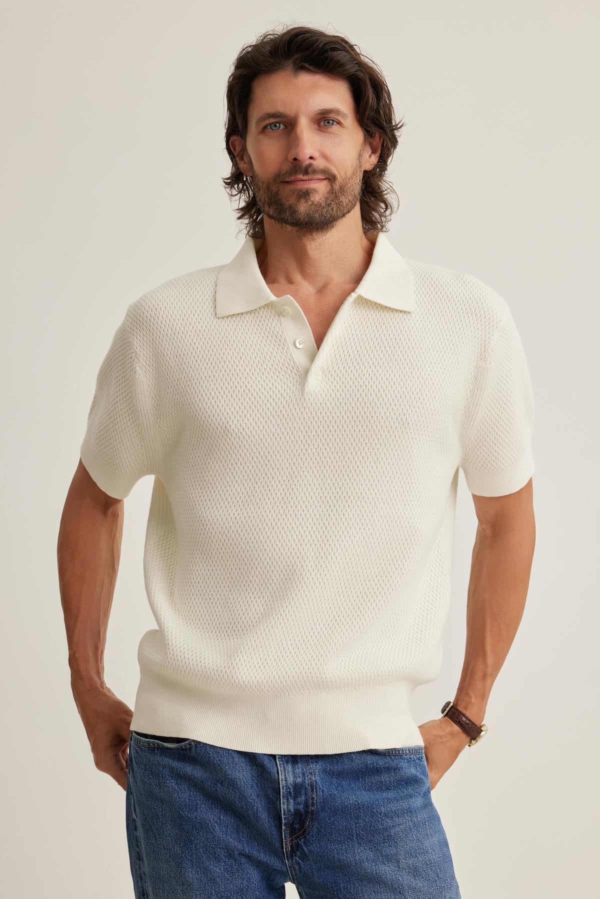 A man with long hair and a beard is wearing the LOWELL Cotton Cashmere Mesh Sweater Polo by Velvet by Graham & Spencer paired with blue jeans, standing with a neutral expression.