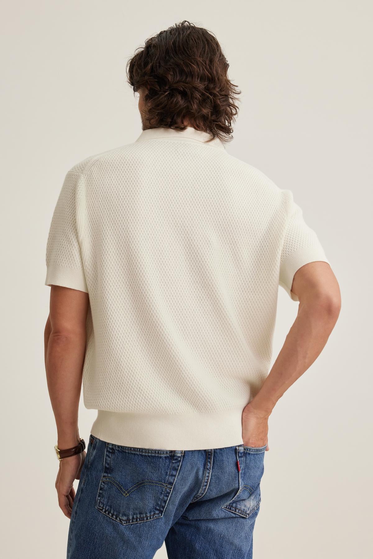 Man with wavy hair wearing Velvet by Graham & Spencer's LOWELL COTTON CASHMERE MESH SWEATER POLO and blue jeans, facing away.
