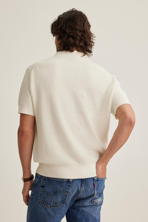 Man with wavy hair wearing Velvet by Graham & Spencer's LOWELL COTTON CASHMERE MESH SWEATER POLO and blue jeans, facing away.