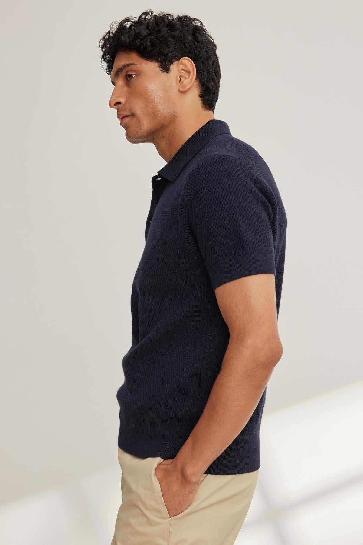 A person stands sideways wearing a LOWELL Cotton Cashmere Mesh Sweater Polo by Velvet by Graham & Spencer and beige pants against a plain background.