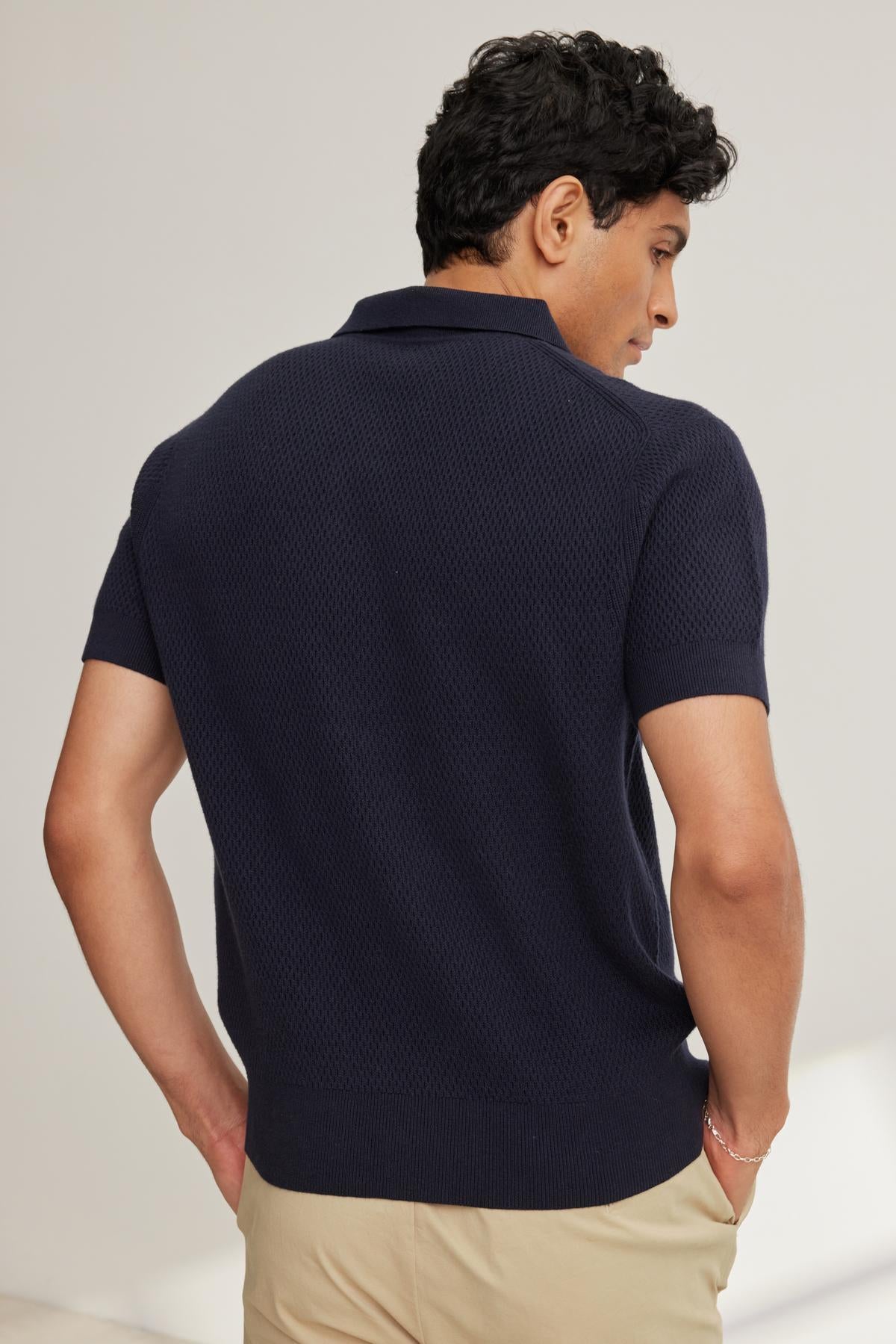A person with short dark hair is seen from behind, wearing a navy LOWELL COTTON CASHMERE MESH SWEATER POLO by Velvet by Graham & Spencer and beige pants.
