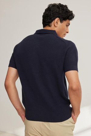 A person with short dark hair is seen from behind, wearing a navy LOWELL COTTON CASHMERE MESH SWEATER POLO by Velvet by Graham & Spencer and beige pants.