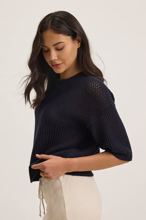 A woman in a relaxed-fit navy VIENNA COTTON CASHMERE MESH SWEATER by Velvet by Graham & Spencer and beige pants looks down against a light background.