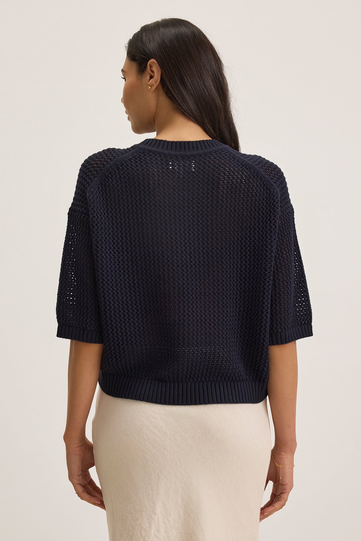 A person with long dark hair wears the VIENNA COTTON CASHMERE MESH SWEATER by Velvet by Graham & Spencer in navy blue and a light beige skirt, standing against a neutral background.-38663172587713