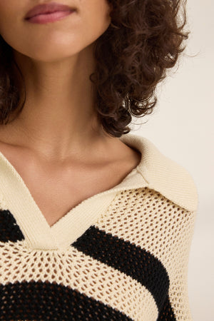 Close-up of a person with curly hair wearing a YORK COTTON CASHMERE MESH SWEATER POLO by Velvet by Jenny Graham, showcasing its polo-style collar and knitted stripes in beige and black.