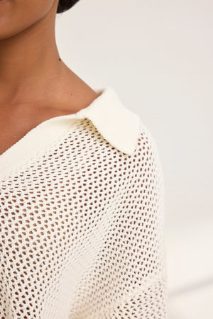 Close-up of a person wearing a YORK COTTON CASHMERE MESH SWEATER POLO by Velvet by Jenny Graham in white, exuding casual charm with its open-knit design that reveals the shoulder and part of the neck against a plain backdrop.
