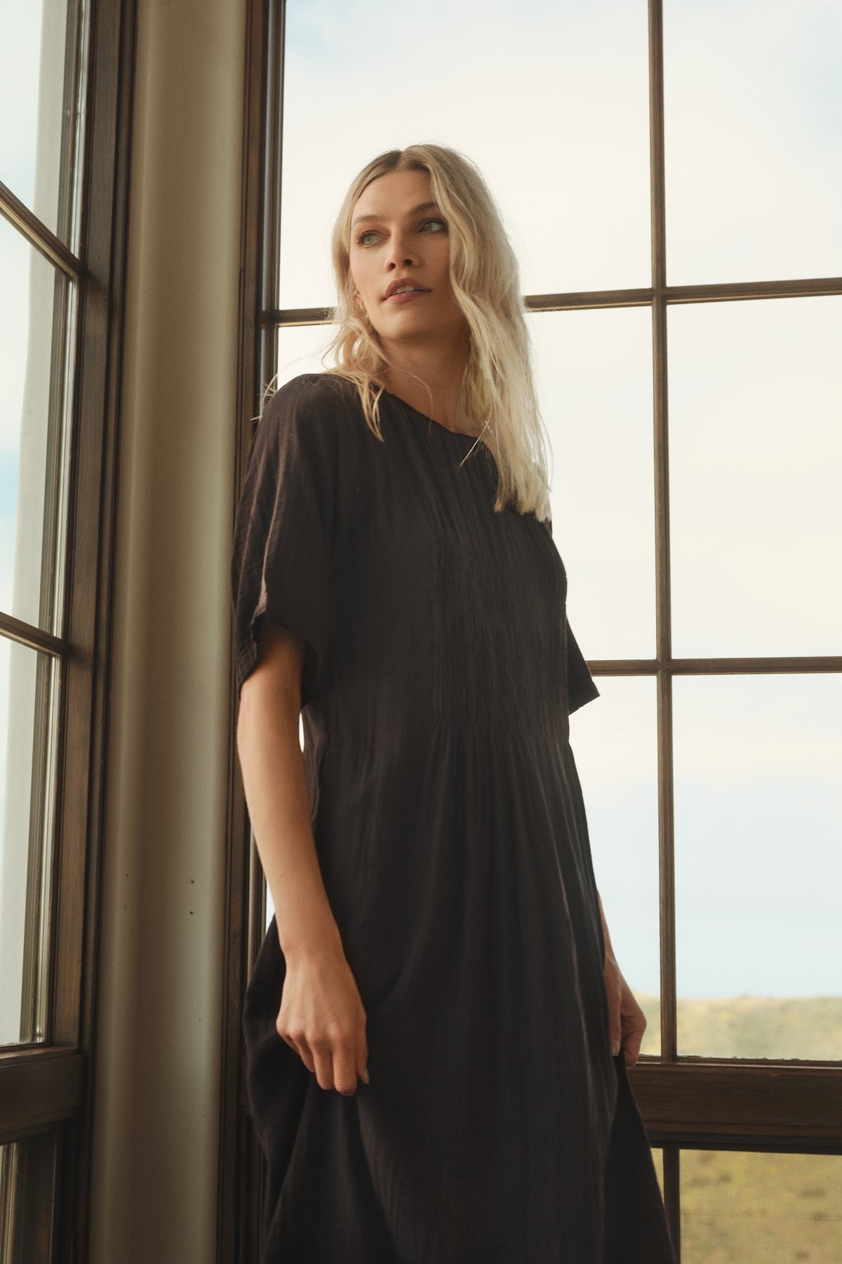 A woman is standing in front of a window wearing the ASHLEIGH COTTON GAUZE MAXI DRESS by Velvet by Graham & Spencer.-35702048325825
