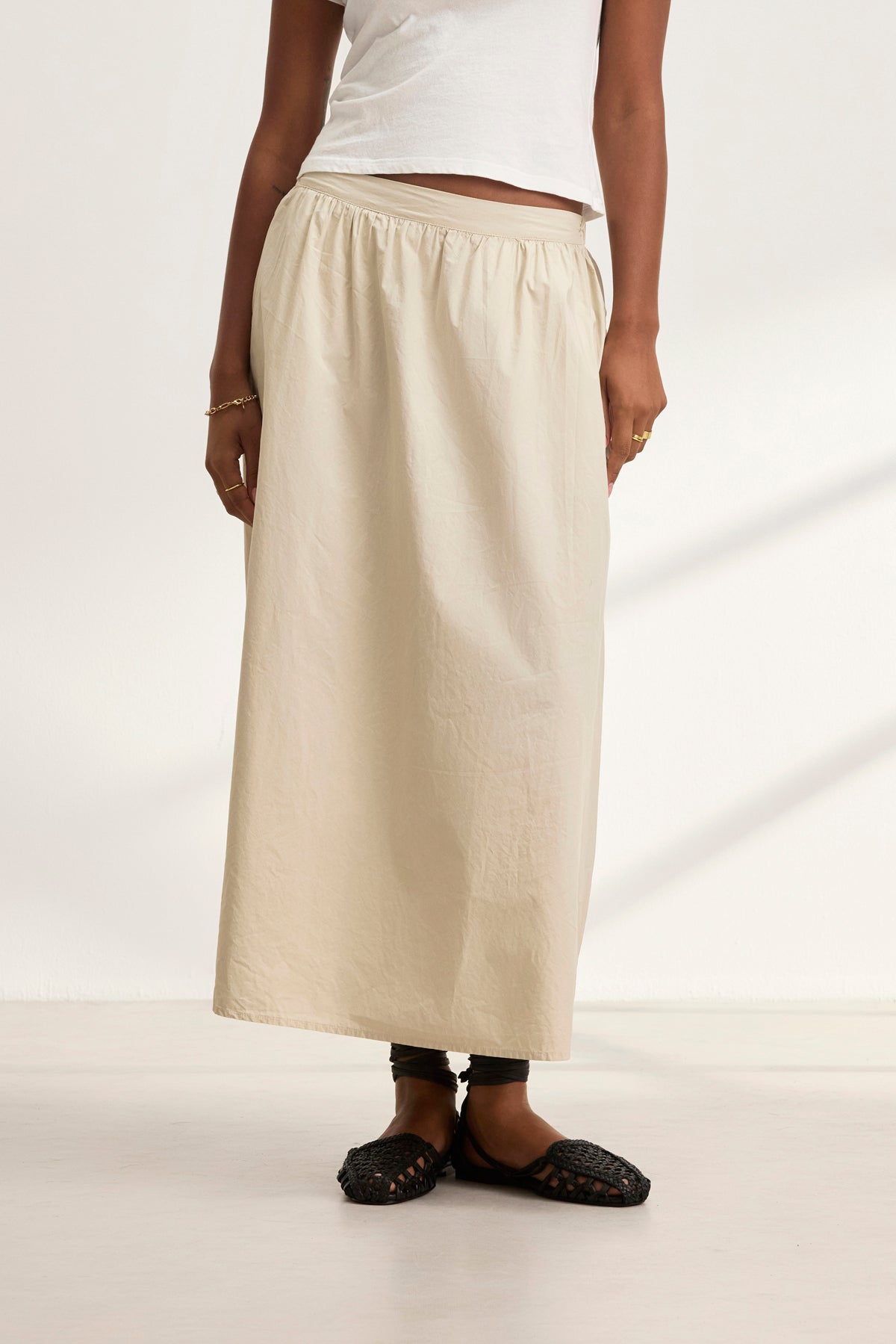 A person stands against a plain background wearing a white top, the BELLA SKIRT by Velvet by Graham & Spencer, and black woven flats.-38957694681281