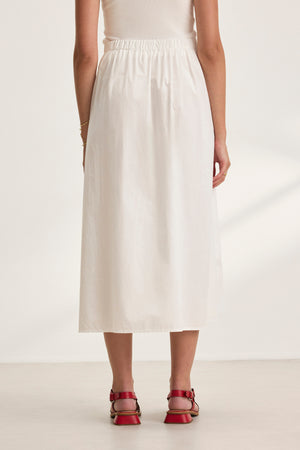 Back view of a person wearing Velvet by Graham & Spencer’s BELLA SKIRT—a plain white cotton poplin A-line skirt—and red sandals on a neutral background.