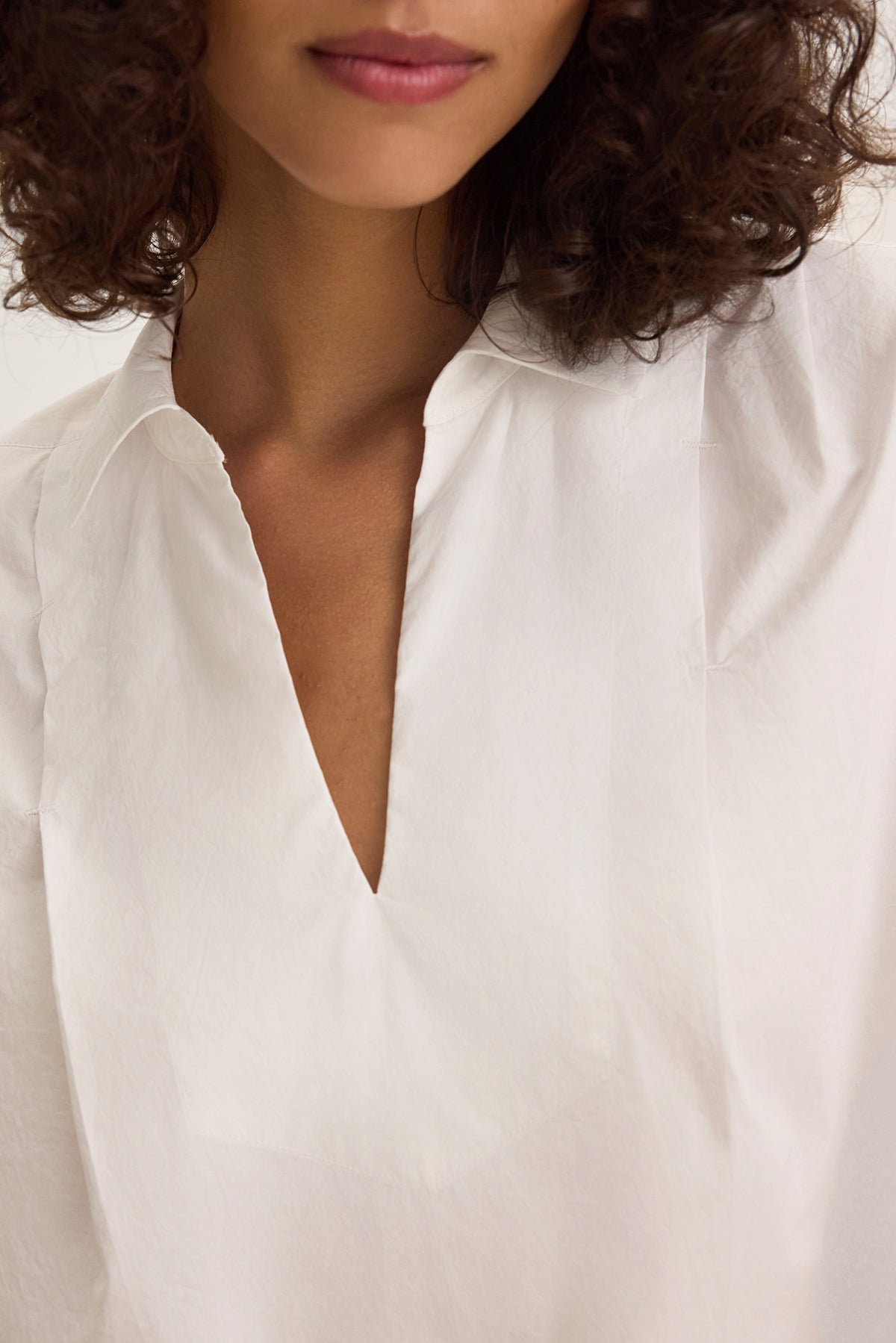 A person is wearing the Velvet by Graham & Spencer FLORENCE TOP in a relaxed fit, white V-neck style, with their curly hair visible, shown from neck to mid-chest.-38662675955905