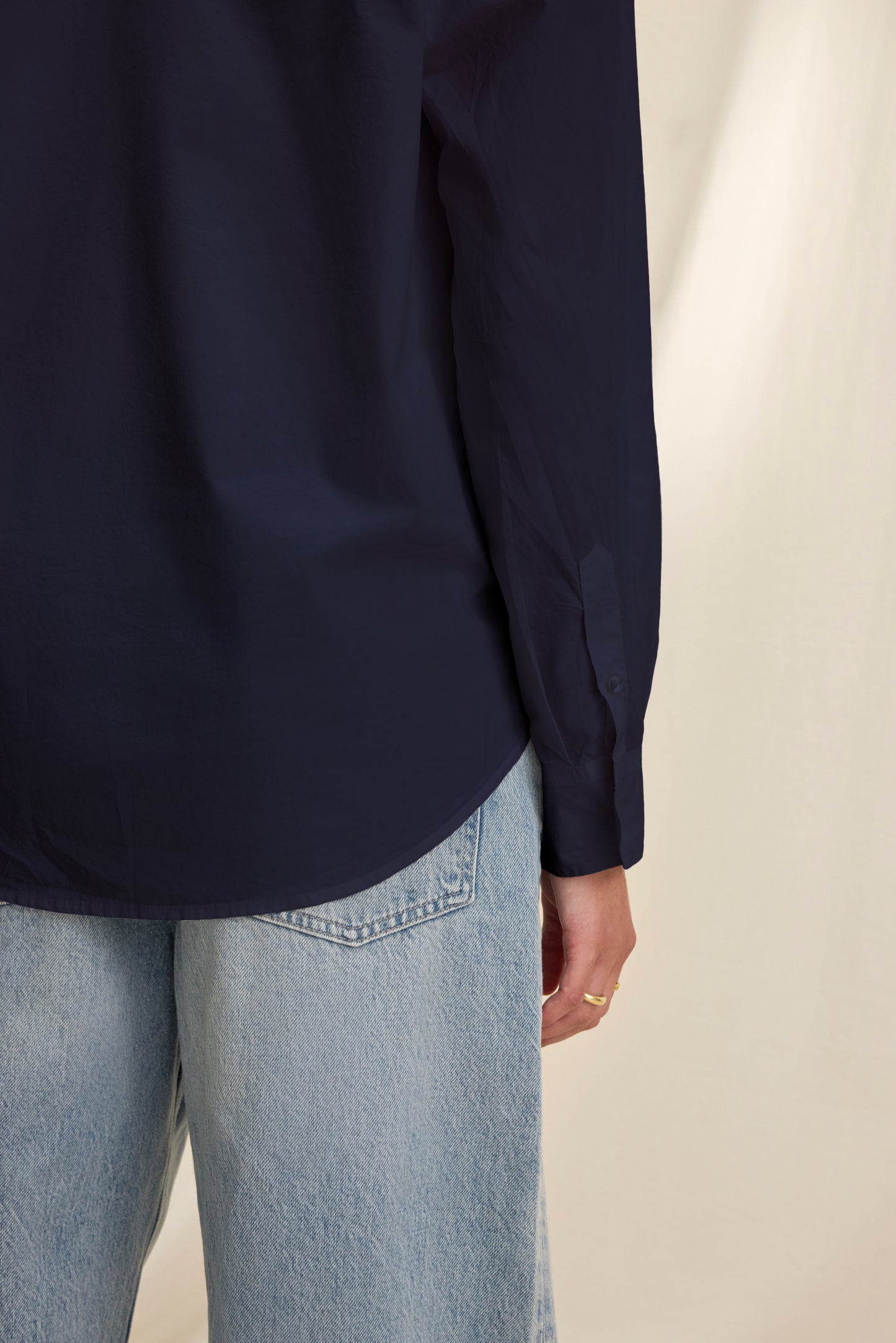Model wearing the KELIA SHIRT by Velvet by Graham & Spencer—a navy blue cotton poplin oversized button-up—paired with light blue jeans, shown from the back and side against a beige background.-40281878397121