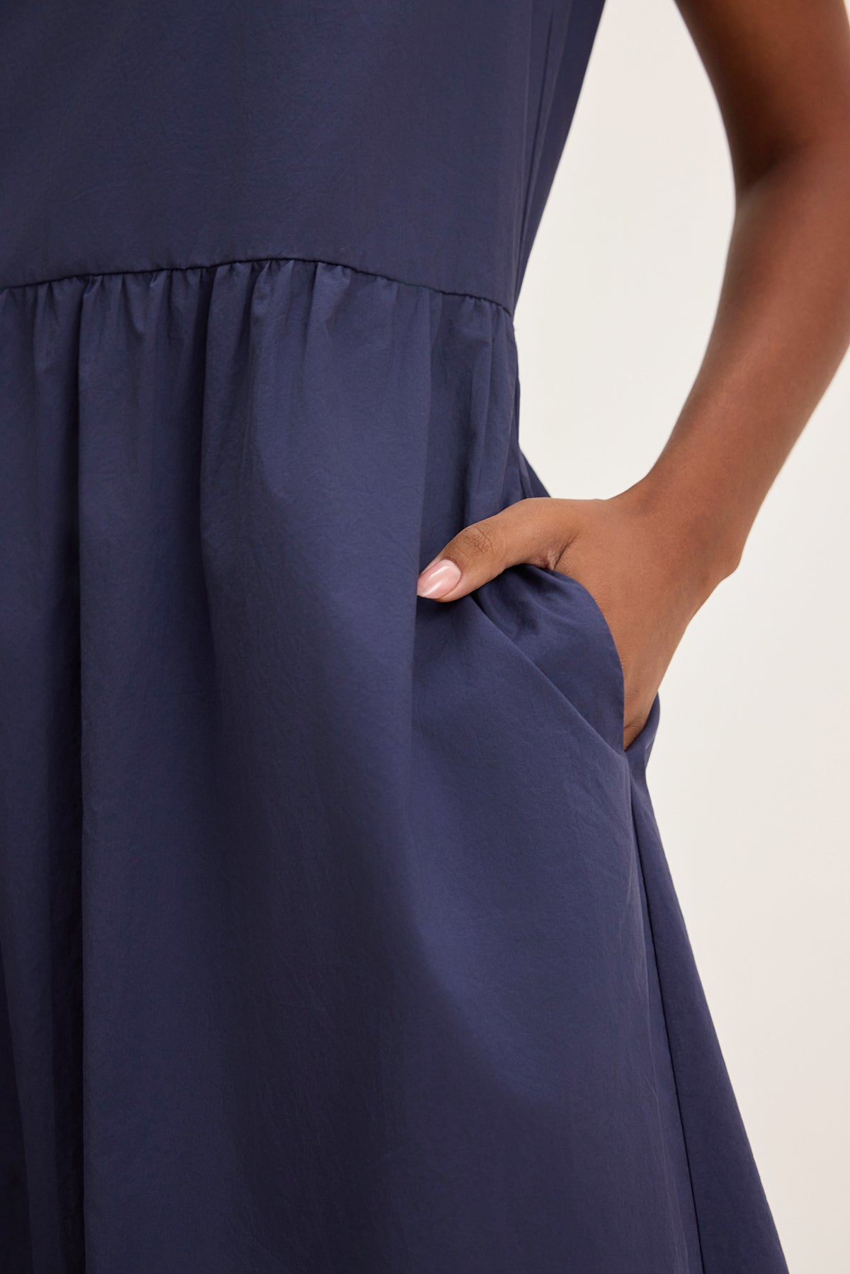 A person wearing the MASHA DRESS by Velvet by Graham & Spencer, a dark blue midi-length dress with an elastic waist, is placing their hand in a side pocket.-38662692634817