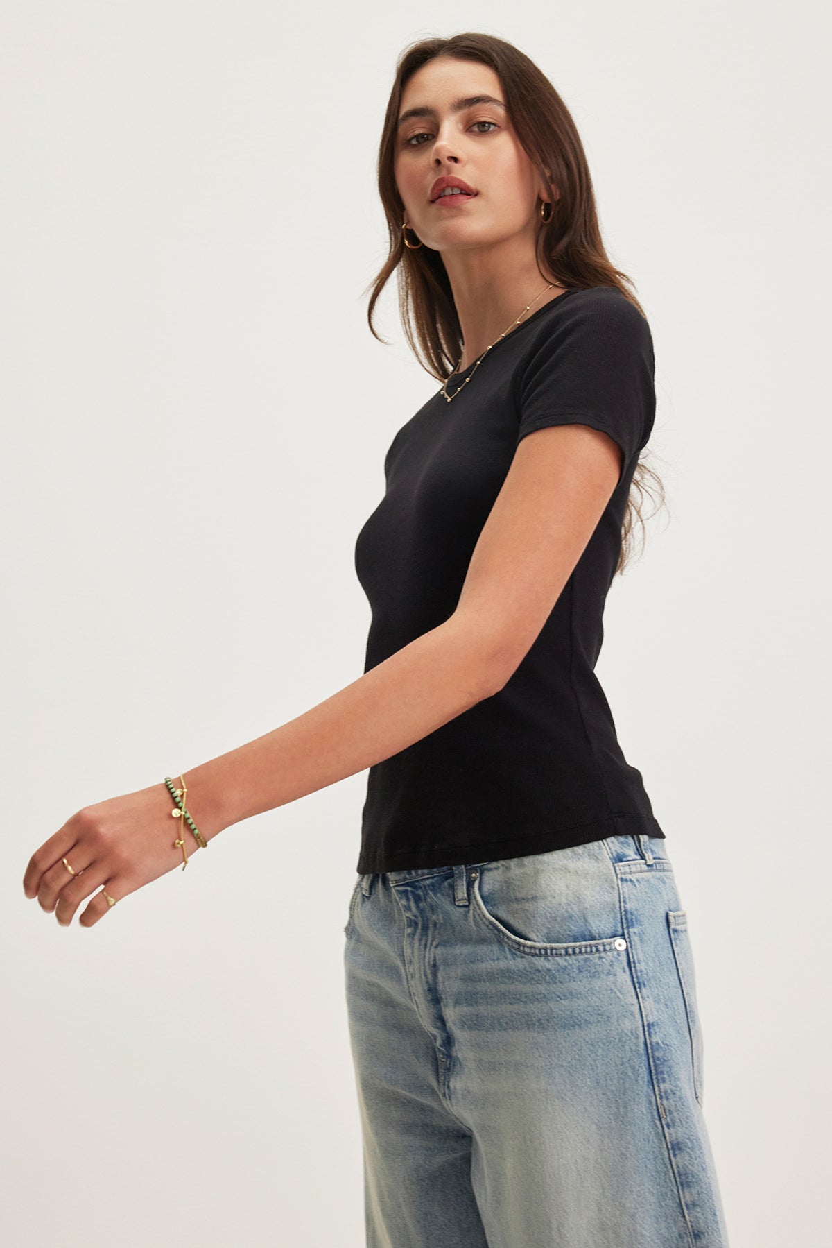 Someone wearing the BRENNY TEE in black by Velvet by Graham & Spencer and blue jeans stands against a plain background.
